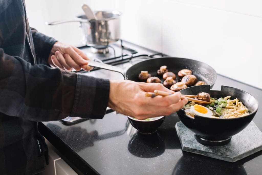 Chef cooking noodles and mushrooms on a stovetop