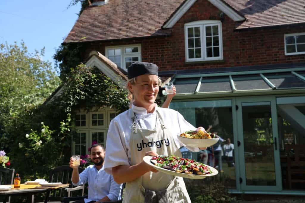 Chef serving plated dishes to guests outside a country house